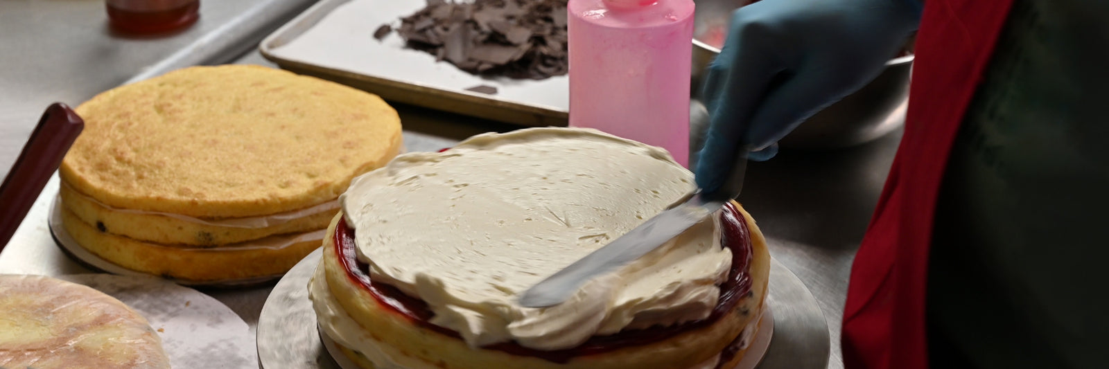 Dilettante Chocolates baker topping raspberry cake with a layer of vanilla frosting