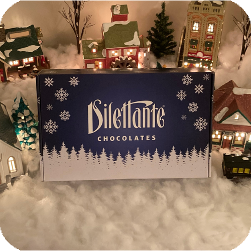 Dilettante Chocolates Snowflake Gift Collection beside a festive holiday village