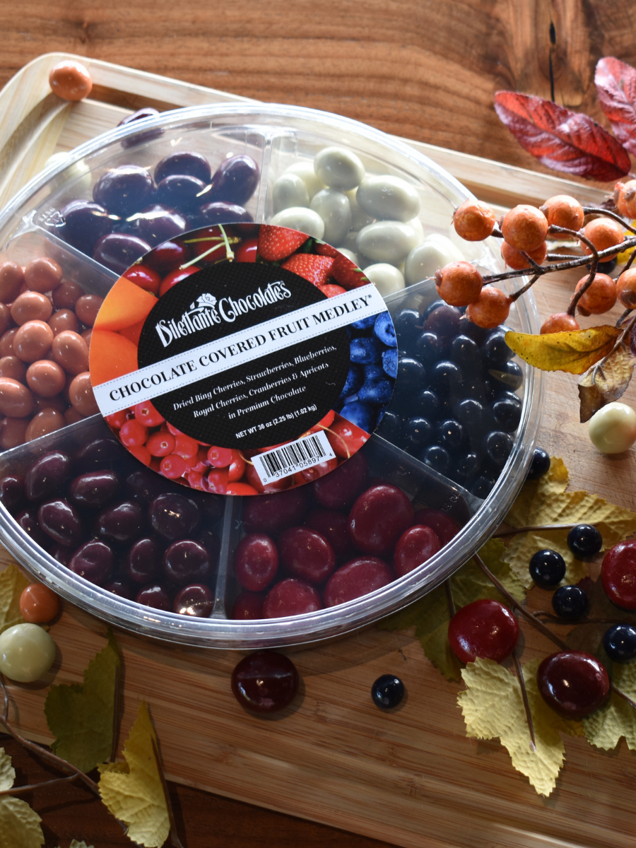 Dilettante Chocolates Fruit Medley Wheel resting on a cutting board and fall decorations. Assortment features blueberries, strawberries, cherries, cranberries, and apricots covered in chocolate