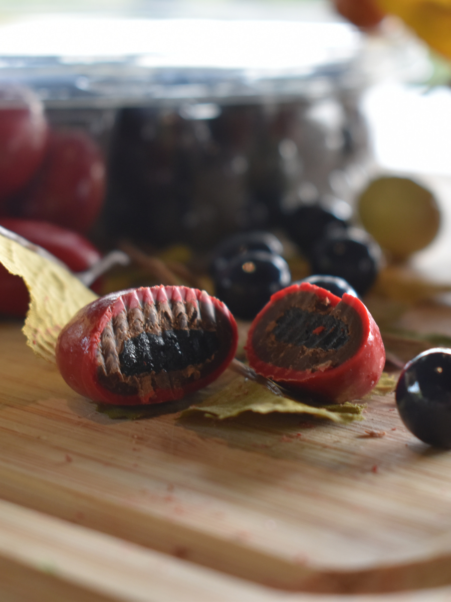 Dilettante Chocolates Chocolate-Covered Royal Cherry cut into two pieces, revealing a dried royal cherry covered in chocolate with a bright red outer shell