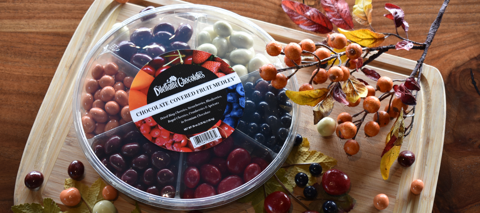 Dilettante Chocolates Fruit Medley Wheel beside fall decorations. Assortment features blueberries, cherries, cranberries, apricots, and strawberries.